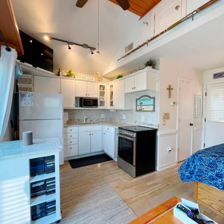 Small kitchen with white cabinets, black stove, microwave, and adjacent bed in a bright, compact studio apartment.