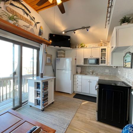 Compact kitchen with white cabinets, black stove, fridge, and microwave, next to a sliding glass door leading to a deck.