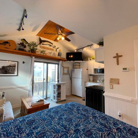 Cozy studio with a bed, kitchenette, sofa, ceiling fan, guitar shelf, and sliding glass door to a balcony.