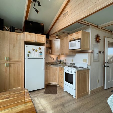 Small kitchen with light wood cabinets, white appliances, a window, and a door leading outside.