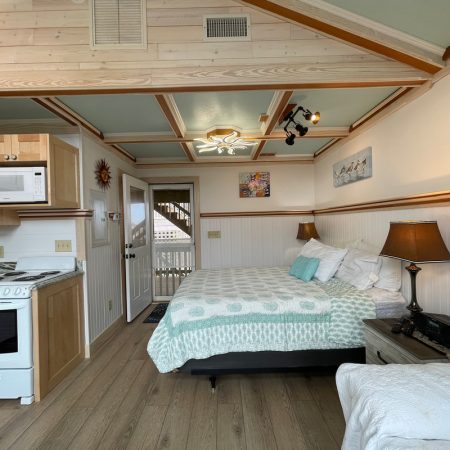 A cozy studio room with a bed, kitchenette, lamps, and a door leading to an outdoor stairway.