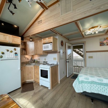 Small studio with a kitchen, bed, and wooden cabinets; door leads to an outdoor staircase.
