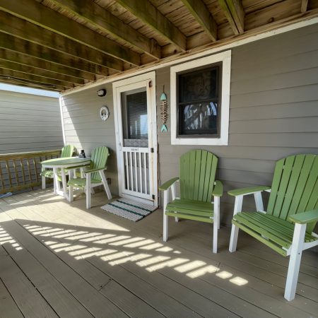 Covered porch with two green chairs, a small table with two chairs, and a white door on a gray house.