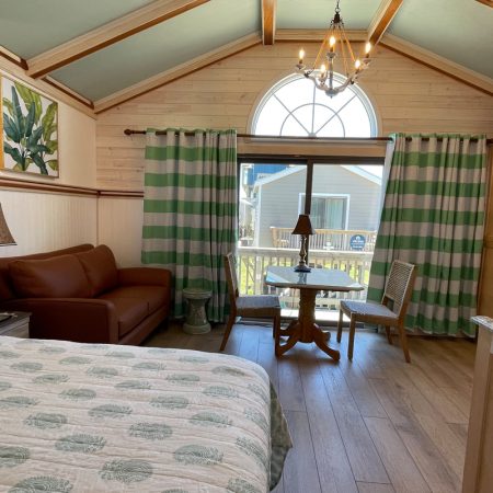 Cozy room with a bed, sofa, small table, two chairs, and large window with green striped curtains and outside view.
