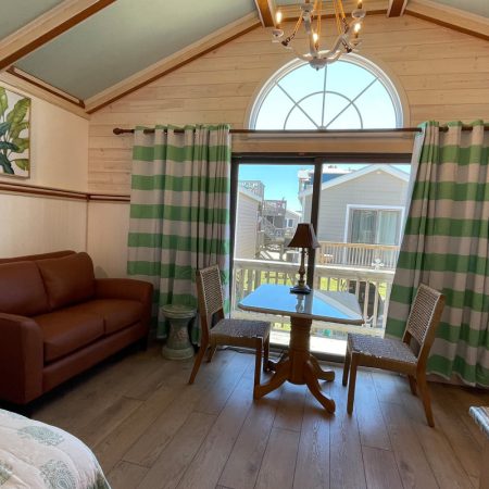 A cozy room with a brown sofa, small table, two chairs, striped curtains, and a large arched window.