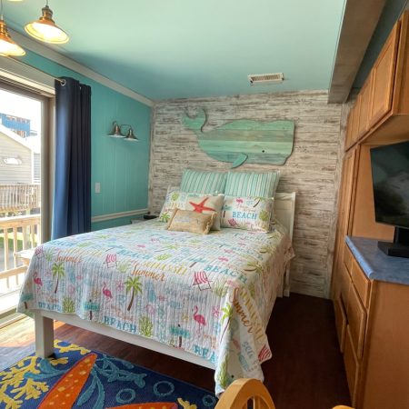 Beach-themed bedroom with whale wall art, colorful bedding, TV, ocean view, and wood accents for a cozy coastal vibe.