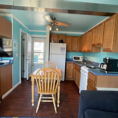 Cozy kitchen with wood cabinets, white fridge, stove, microwave, coffee maker, and small dining table with chairs.