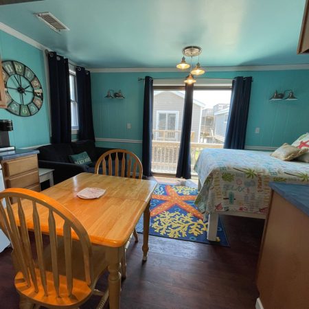 Small studio with a bed, dining table, sofa, kitchen area, and glass doors leading to a deck outside.