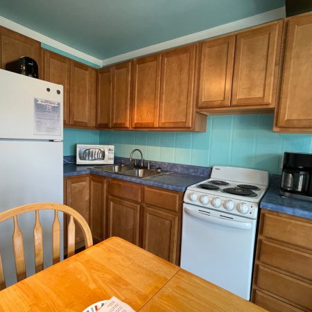 Small kitchen with wooden cabinets, white appliances, a coffee maker, microwave, toaster, and a wooden dining table.