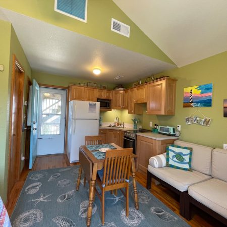 Small kitchen and dining area with light wood cabinets, green walls, sofa, and beach-themed decor in a cozy room.
