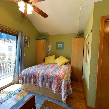 Bedroom with a double bed, colorful quilt, yellow pillows, wood furniture, and sliding glass door to a balcony.