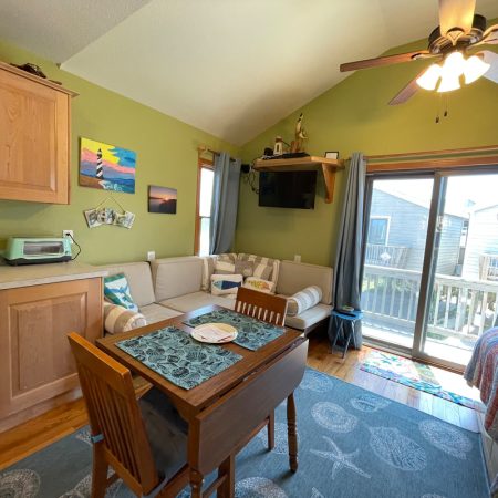 Small living area with green walls, dining table, couch, TV, kitchen appliances, and sliding glass door to a balcony.