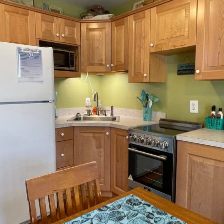 Small kitchen with wooden cabinets, white fridge, sink, stove, microwave, toaster, and green walls. Dining table in front.