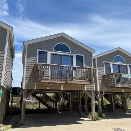Three elevated beach houses with wood balconies and parking underneath on a sunny day.