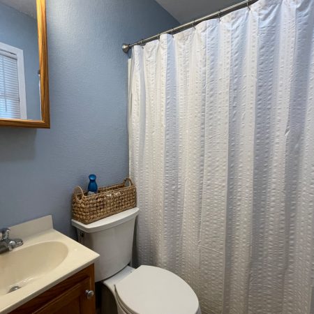 Small bathroom with a sink, mirror, toilet, wicker basket, blue wall, and white shower curtain.