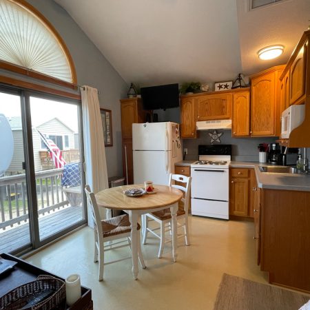 Cozy kitchen with wooden cabinets, round table, white appliances, next to a deck displaying an American flag.