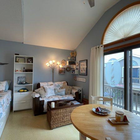 Cozy room with a bed, loveseat, bookshelf, round dining table, and sliding door leading to a balcony with a house view.
