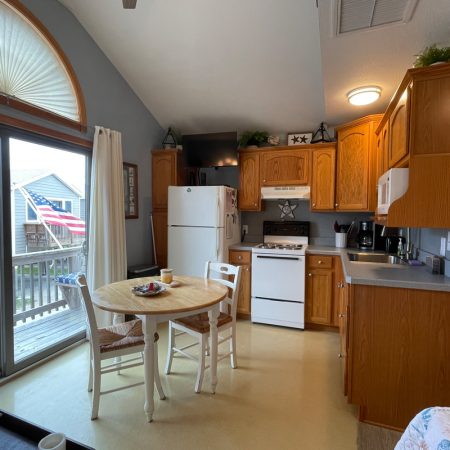 Small kitchen with wooden cabinets, white appliances, a round dining table, and a sliding glass door leading to a deck.