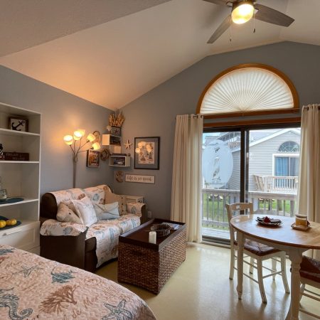 Cozy living space with a sofa, bookshelf, round dining table, and large window with outdoor view.