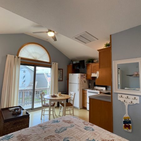 Small kitchen and dining area in a cozy studio with a bed, balcony door, and vaulted ceiling.