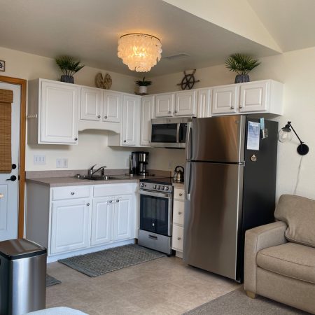 Small kitchen with white cabinets, stainless appliances, and a beige sofa in a cozy, well-lit space with simple decor.