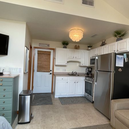 Small modern kitchen with white cabinets, stainless steel appliances, and a wall-mounted TV next to a beige sofa.