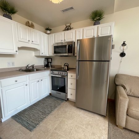 Small kitchen with white cabinets, stainless steel appliances, and a beige sofa partially visible on the right.