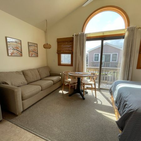 Bright room with a sofa, small dining table, bed, and large window overlooking a balcony and neighboring house.