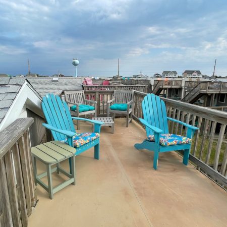 Rooftop deck with four turquoise chairs, floral cushions, small green table, and cloudy sky in the background.