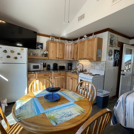 Small kitchen and dining area with wooden cabinets, round table, and a bed partially visible on the right side.