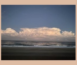 Calm ocean waves under a blue sky with large, fluffy clouds on the horizon.