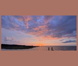 Sunset over a calm body of water with pink and purple clouds scattered across the sky.