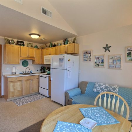 Small kitchen and living area with light wood cabinets, a sofa, a round table, and beach-themed wall decor.