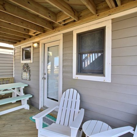 Wooden deck with two white Adirondack chairs, a small round table, a picnic table, and a door with a window.