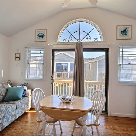 Small dining area with round table and chairs, couch, and large windows overlooking neighboring houses.