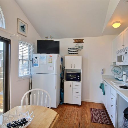 Small, bright kitchen with white cabinets, appliances, a round table, and a door leading to an outdoor deck.