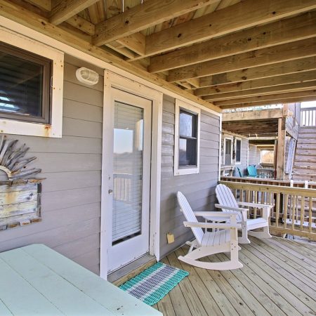 Covered wooden porch with two white rocking chairs, a table, and coastal decor on the wall.