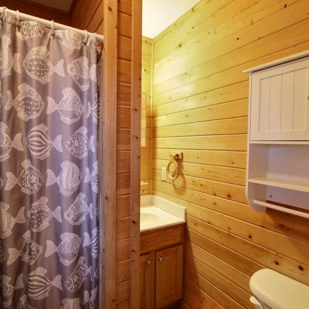 Small bathroom with wood-paneled walls, a white cabinet, toilet, sink, and a shower with a fish-patterned curtain.