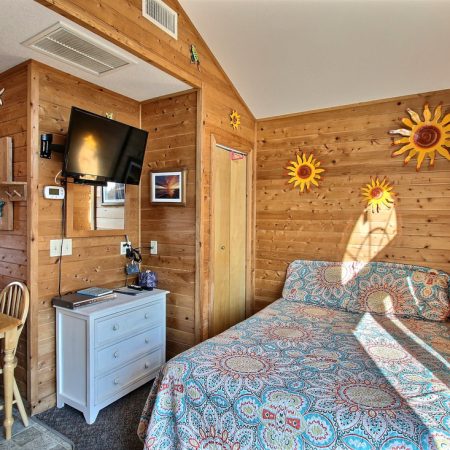 Cozy wood-paneled room with a bed, TV, small dining table, dresser, and sun decorations on the wall.