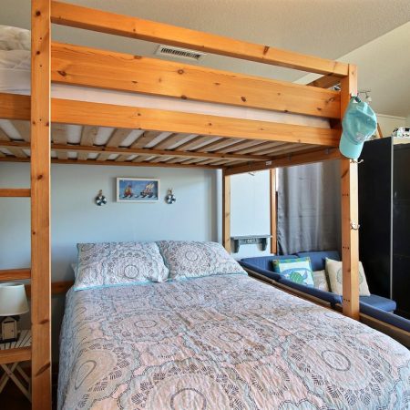 Wooden loft bed above a double bed with patterned bedding in a neatly arranged bedroom with light blue walls.