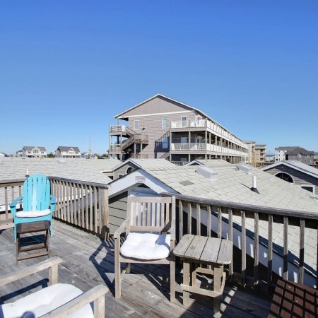 Rooftop deck with chairs and table overlooking neighboring buildings under a clear blue sky.