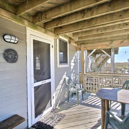 Covered wooden porch with a table, chairs, and a screen door; view of stairs and other decks in the background.
