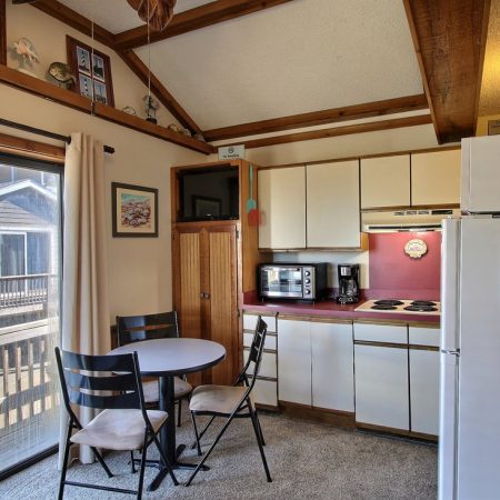 Small kitchen with white cabinets, round table with three chairs, appliances, and sliding glass door to a balcony.
