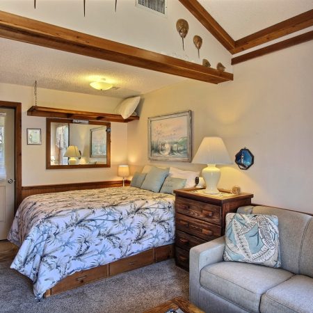 Cozy bedroom with a double bed, wooden beams, a dresser, a sofa, and sunlight coming through lace curtains.