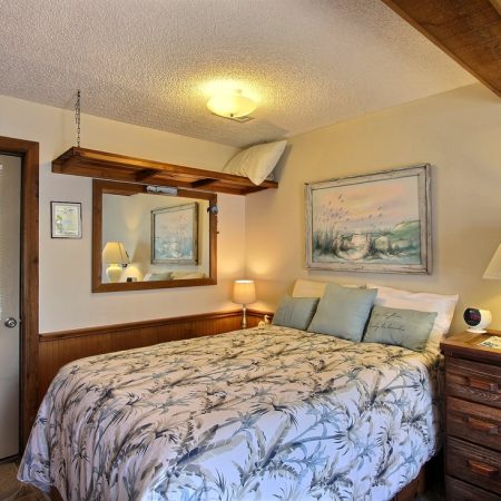 Cozy bedroom with a double bed, floral bedding, wooden dresser, lamps, wall art, and a mirror above the bed.