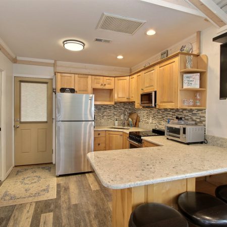 Small kitchen with wood cabinets, stainless steel appliances, bar counter with stools, and a wall-mounted TV.